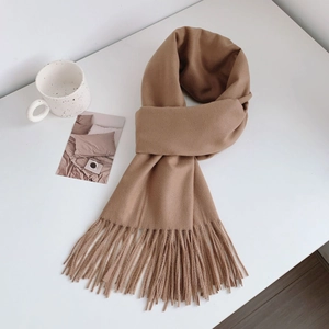 Close-up of soft light brown cashmere-like scarf with fringe details on a white surface