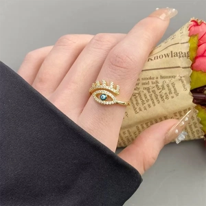Close-up of golden Evil Eye ring with white zircons and blue enamel on a female hand