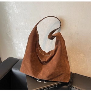 Close-up of a dark brown suede hobo bag with zipper and wide shoulder strap on a book