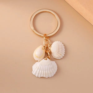 Golden keychain with natural white shells and spiral shell pendant on beige background