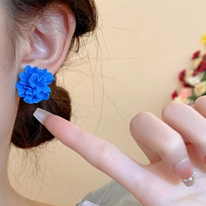 Gros plan de boucles d'oreilles fleurs bleu Klein en résine portées sur l'oreille