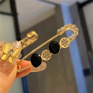 Detail of a golden safety pin brooch featuring black oval stones and sparkling crystals