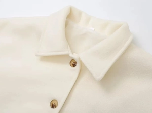 Close-up of lapel and amber-patterned buttons on a cream wool coat with premium texture