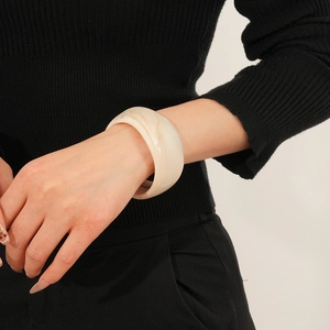 Close-up of a wide marbled cream resin bangle worn on a model against black knitwear