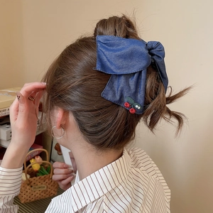 Close-up of a blue denim bow hair clip with detailed red cherry embroidery on a bun hairstyle