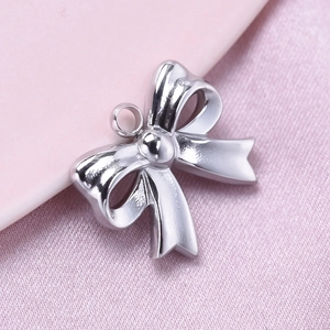 Close-up of polished silver bow pendant accessory on soft pink silk background