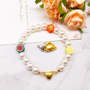 Detail of gold and silver heart-shaped magnetic clasps on a white pearl charm bracelet