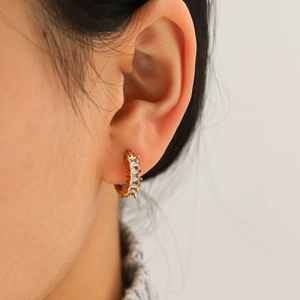 Boucles d'oreilles créoles dorées en acier titane avec zircons cubiques sur un modèle