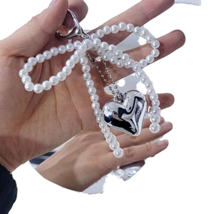 Cute faux pearl bow bag charm with silver heart pendant and lobster clasp hanging