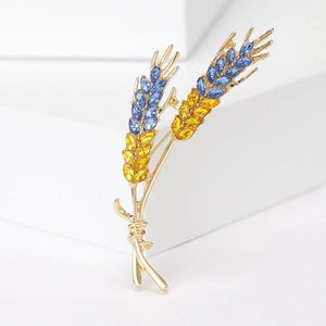 Detailed view of wheat brooch with blue and yellow crystals on white geometric stand