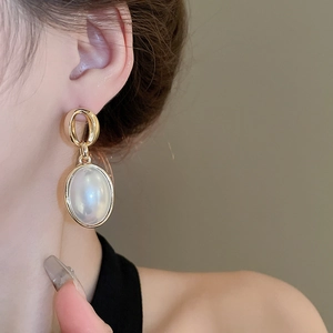 Close-up of vintage gold oval faux pearl earrings worn by a model in soft lighting