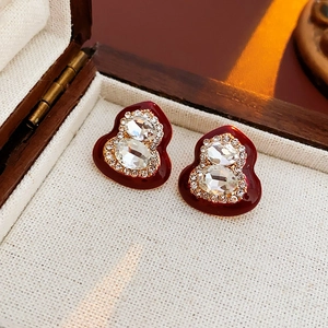 Detailed close-up of red enamel gourd stud earrings with sparkling crystals in a wooden box