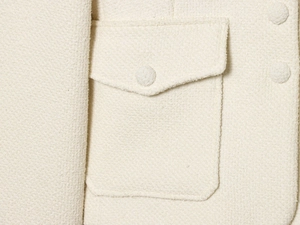 Dettaglio macro del tessuto in tweed bianco panna con tasca a patta e bottone coordinato