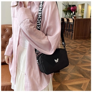 Detail of nylon crossbody bag featuring silver butterfly and lettered wide strap