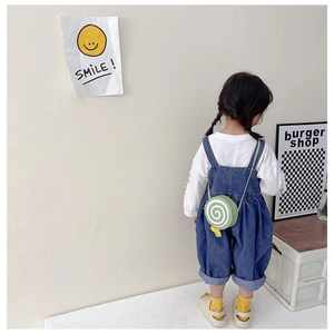 Rear view of a child wearing a green snail-shaped crossbody bag and denim overalls