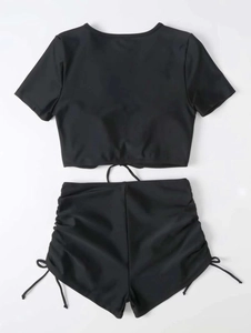 Flat lay of black two-piece swimsuit featuring ruched drawstring high-waisted shorts