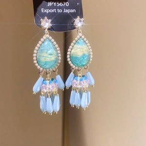 Detail of drop-shaped blue stone earrings with pearl borders and colorful bead tassels