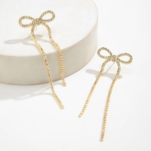 Detailed view of gold bow earrings with sparkling white crystals and long tassel fringe