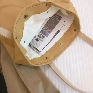Detail of mustard yellow canvas tote bag with a metallic snap button and white lining