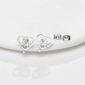 Close-up of heart-shaped hollow earrings with musical note motif on white ceramic