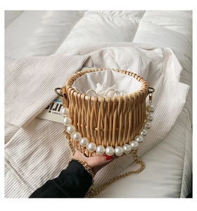 Detail of woven straw bag featuring elegant pearl strap and metal chain on white bedding