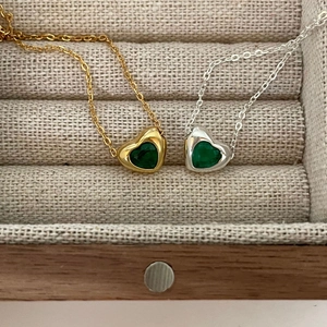 Close-up of gold and silver heart necklaces with green gemstones in a jewelry box