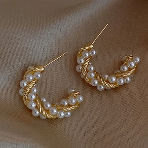 Close-up of elegant gold twisted C-shaped earrings with inlaid white pearls
