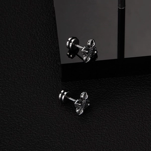 Macro shot of vintage punk cross earrings with screw back on a black leather surface
