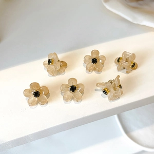 Mini champagne flower hair claws with black crystal center on white geometric background