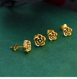 Macro shot of gold rose earrings with detailed petals on a dark green textured background