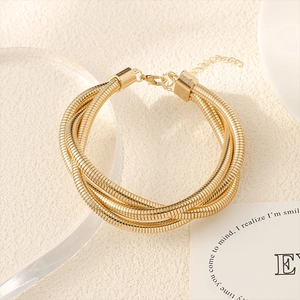 Detail of multi-layer gold snake bone bracelet with lobster clasp on beige tray