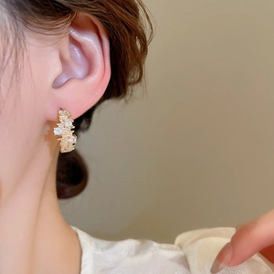 Detailed close-up of a golden wavy ear cuff with sparkling zircons worn by a model
