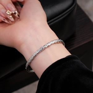 Détail d'un bracelet tissé argenté orné de zircons portés au poignet féminin