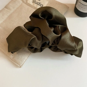 Detail of olive green pleated satin hair claw clip with glossy silk fabric texture
