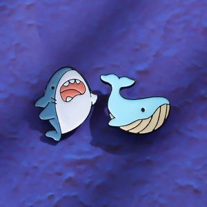 Detail view of cartoon enamel pins featuring a cute blue shark and a smiling whale