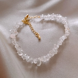 Dettaglio del bracciale in cristallo irregolare con chiusura dorata su fondo di seta