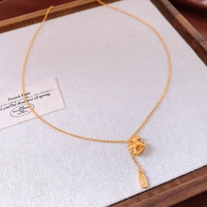 Close-up of gold-plated necklace featuring a rocking horse and coin pendant on linen