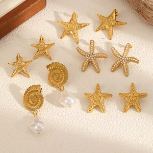 Golden starfish and conch seashell earrings set with pearls on a rustic stone surface