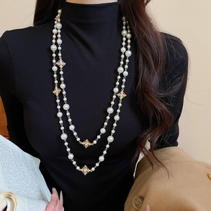 Detailed view of double-layer pearl necklace with sparkling gold cross pendants on black fabric