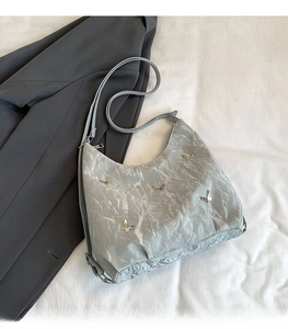 Detail of light grey pleated shoulder bag with metallic butterfly accents and strap