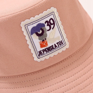 Close-up of pink cotton bucket hat with stamp-style embroidery and French text detail