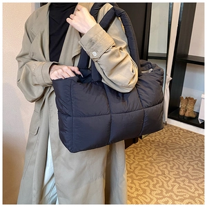Detail of black quilted tote bag with padded texture and wide shoulder straps on model