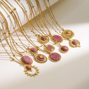 Detalle de collares dorados con piedras rosas y colgantes celestiales sobre soporte blanco