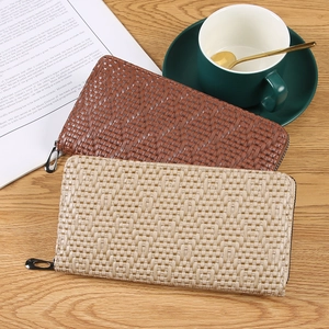 Brown and beige woven leather zip wallets on a wood desk with lifestyle props