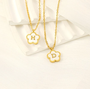 Detail of clover necklaces featuring white petals and golden letters H and D on white fabric