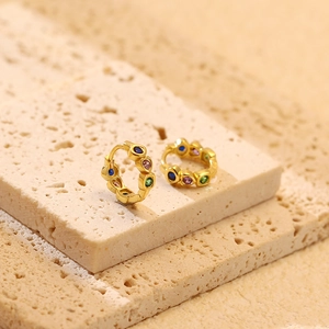 Macro detail of gold hoop earrings with multi-colored gemstones on a textured stone base