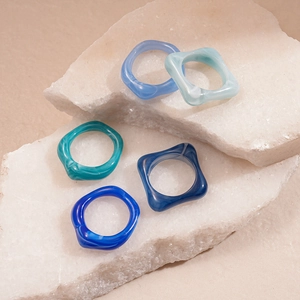 Ensemble de cinq bagues géométriques en acrylique bleu et vert sur socles en pierre