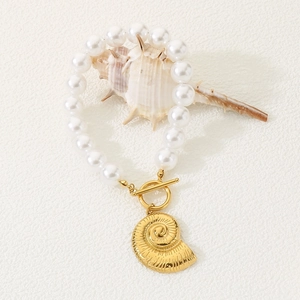 Detailed macro of gold shell pendant and pearl bracelet with OT clasp on beach decor
