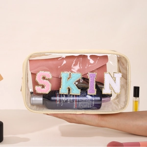 Detail of transparent PVC makeup bag with SKIN glitter patches and beige fabric trim