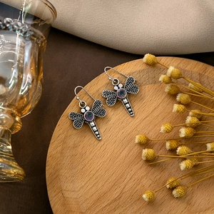 Detail of vintage silver dragonfly earrings with colorful stones on a wooden tray